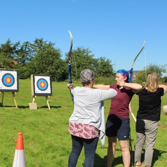 Young people and volunteers doing archery outdoors