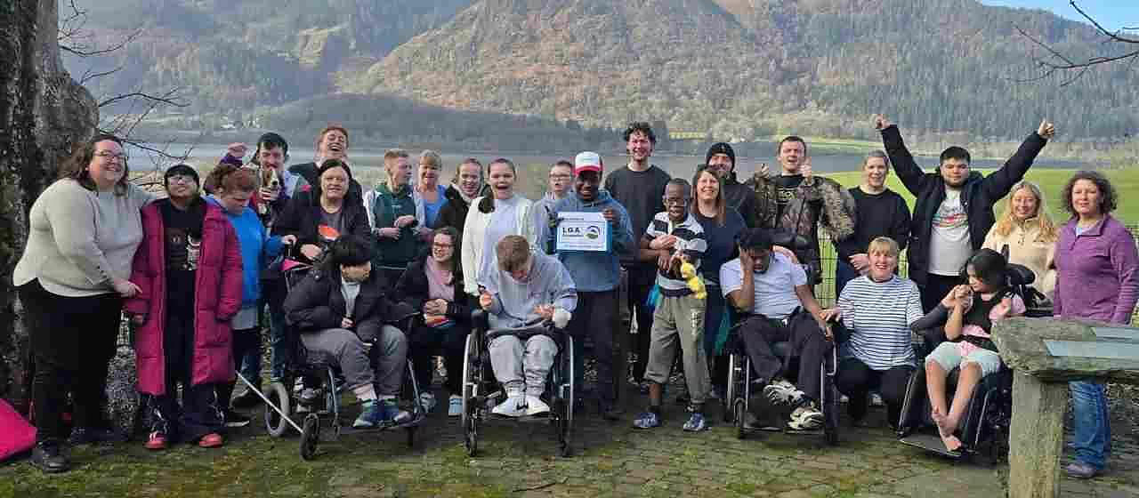 A large group of people, several using wheelchairs, gathered outdoors in front of a hillside