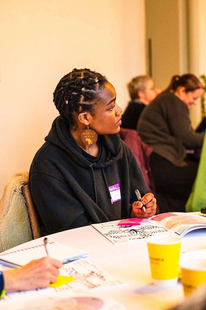 A young woman sitting at a workshop table with printed materials in front of her
