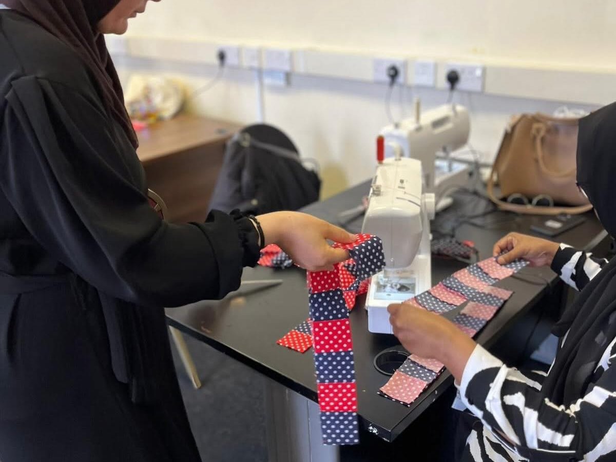 Women at sewing machines, one holding up a strip of patterned fabric