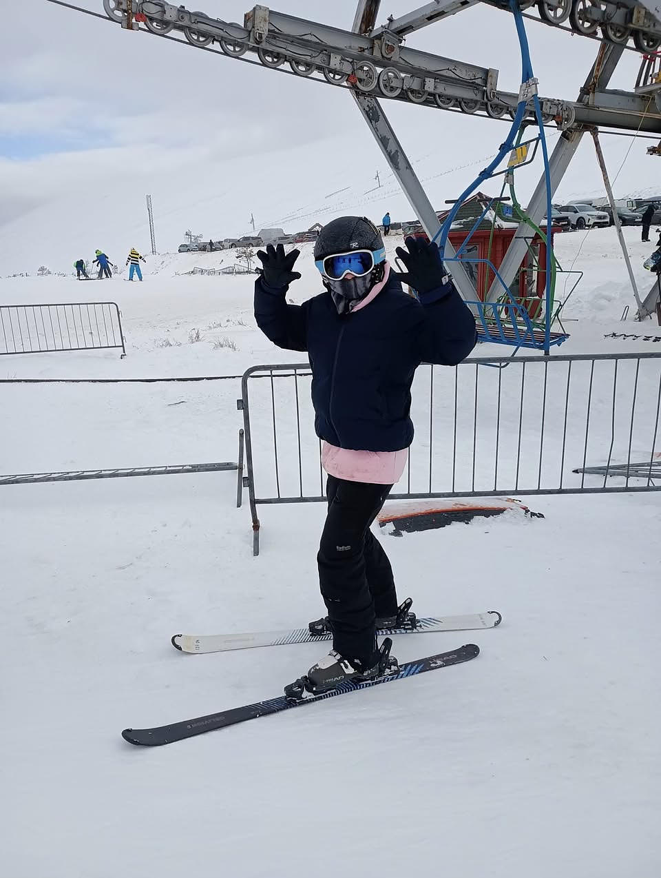 A young person in ski gear and goggles standing on skis in the snow beside a ski lift