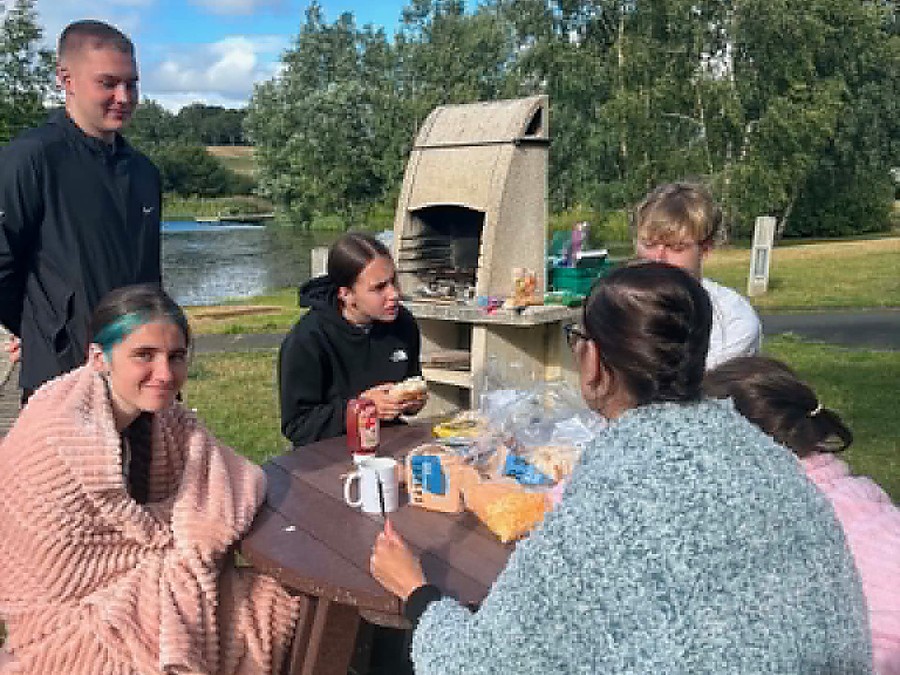 Young people and leaders gathered around a picnic table beside the water