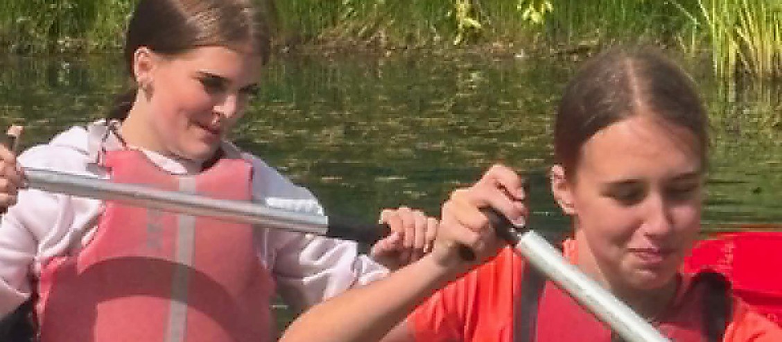 Two young people paddling a canoe together in buoyancy aids during a residential outdoor activity camp