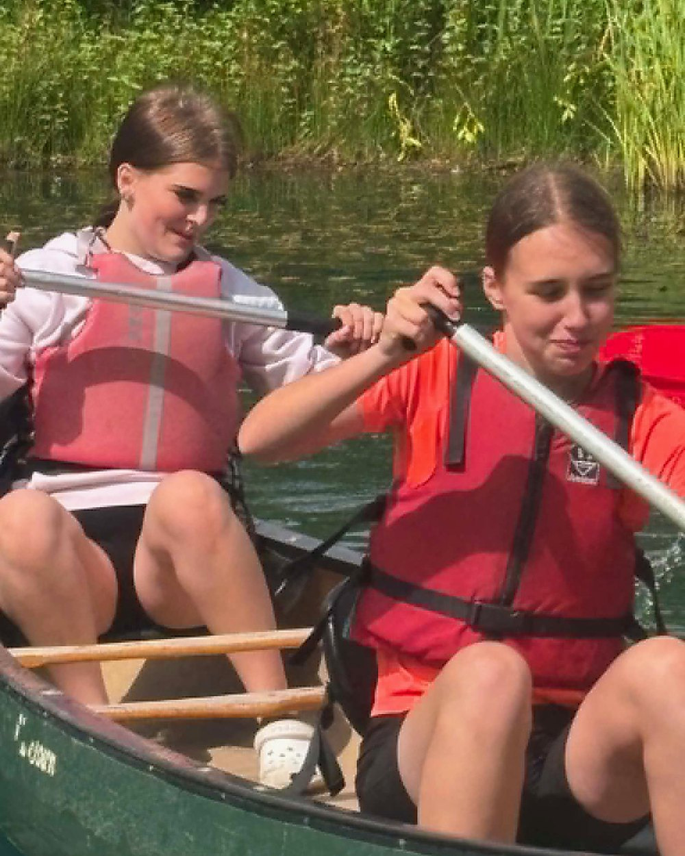 Two young people in buoyancy aids paddling a canoe together on open water