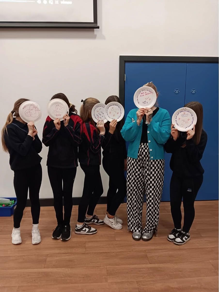 A group of young people standing in a hall holding paper plates in front of their faces