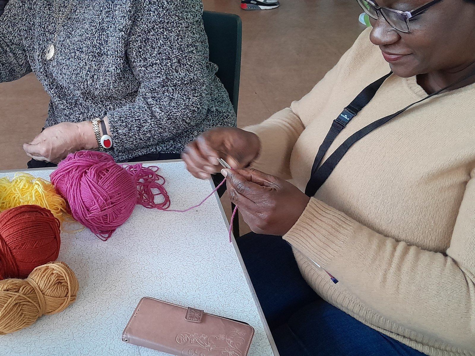 Women knitting at a table covered in balls of brightly coloured wool