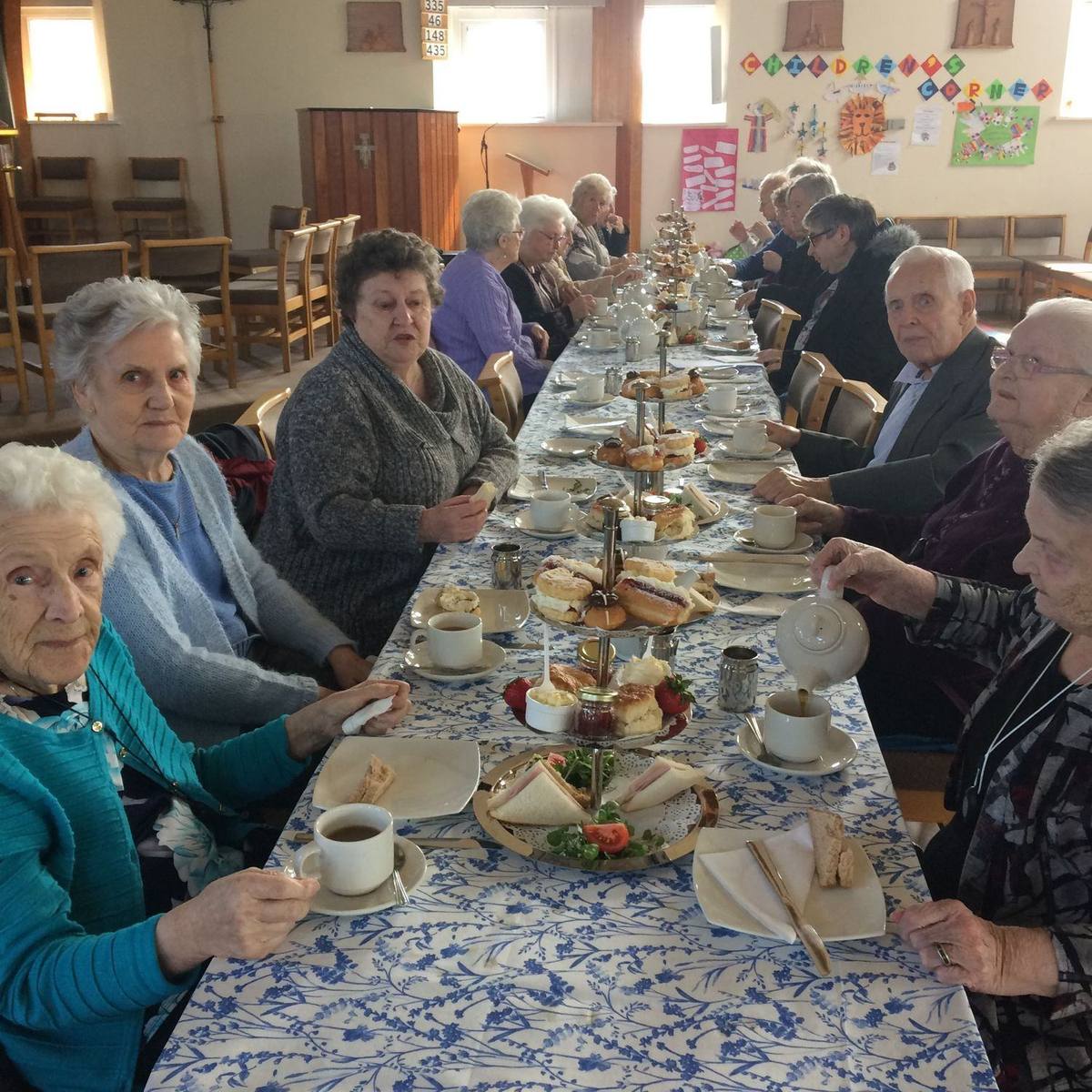 Older neighbours seated at a long table for an afternoon tea